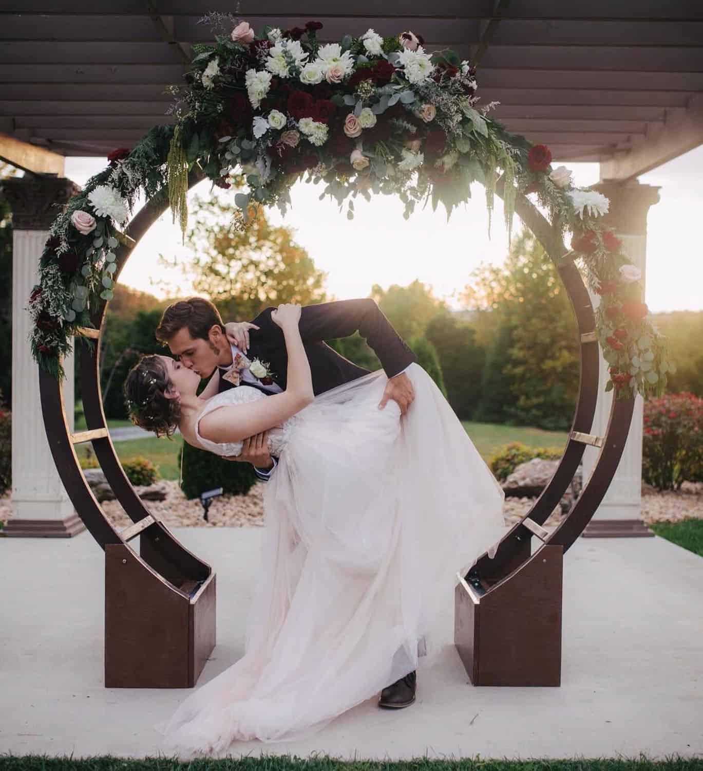 Couple kissing under floral arch at Mountain Ridge Venue during sunset.