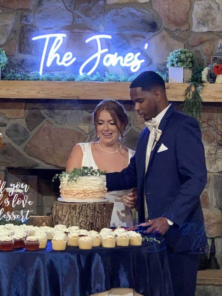 Couple cutting wedding cake at Mountain Ridge Venue with neon sign background.